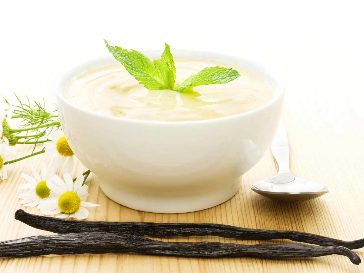 A white bowl of vanilla yogurt with vanilla pods and flowers