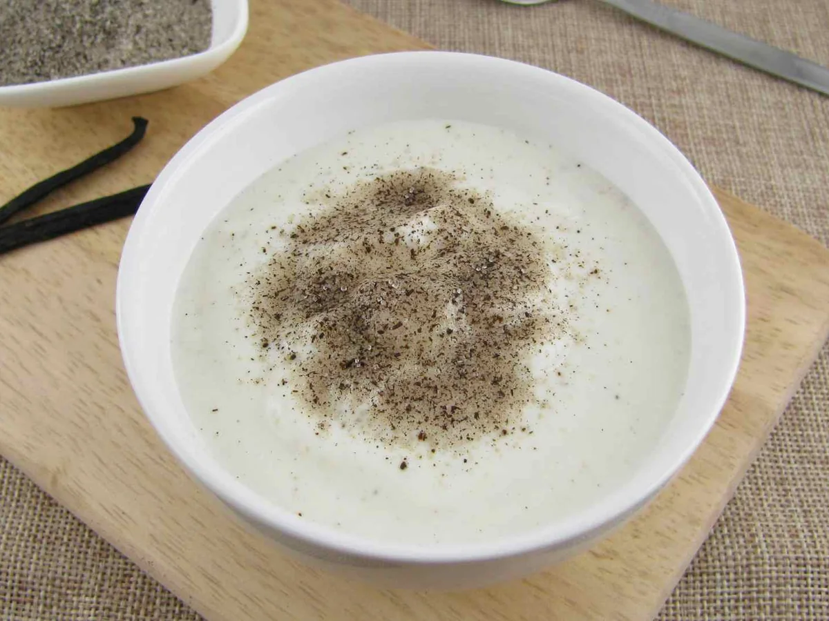 A white bowl of speckled yogurt beside vanilla pods
