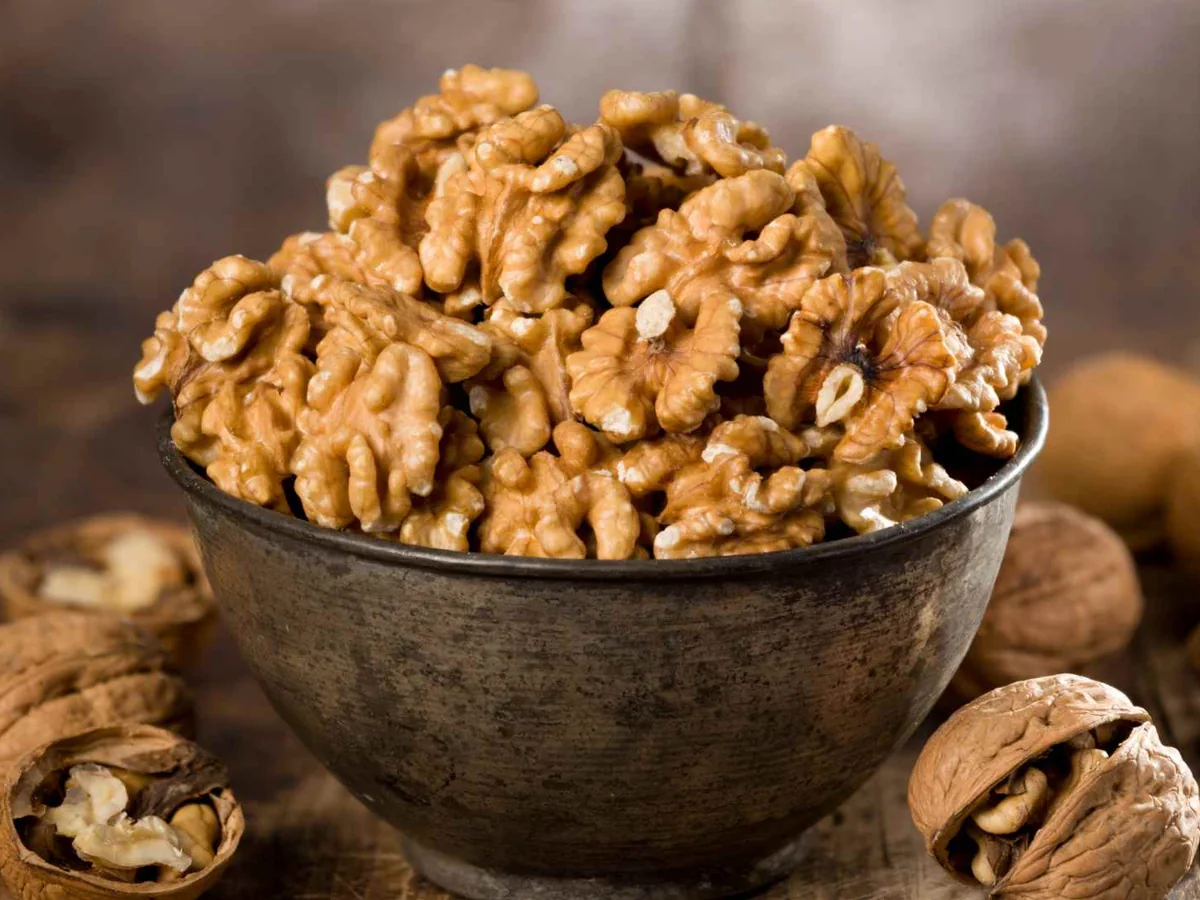 Walnut halves in a dark bowl surrounded by whole walnuts
