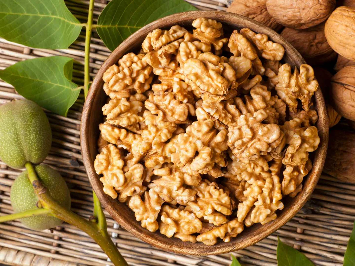 Walnut halves in a bowl beside green leaves and whole walnuts