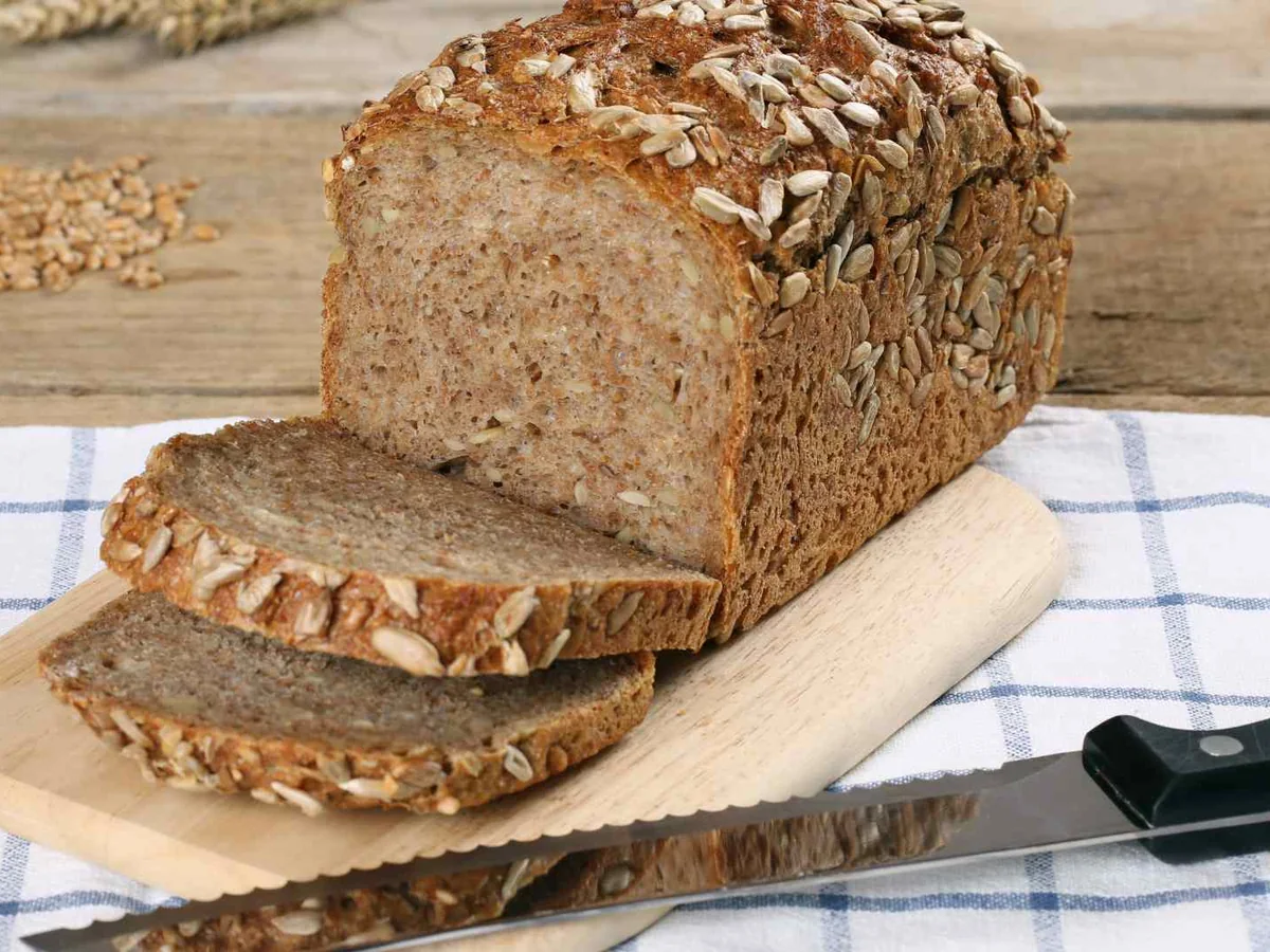 A sliced loaf of seeded whole wheat bread on a wooden board