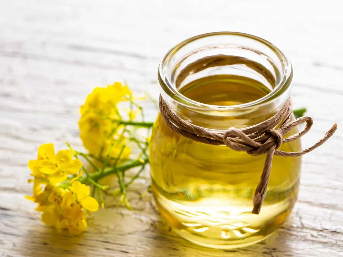 Pale cooking oil in a glass jar beside yellow flowers