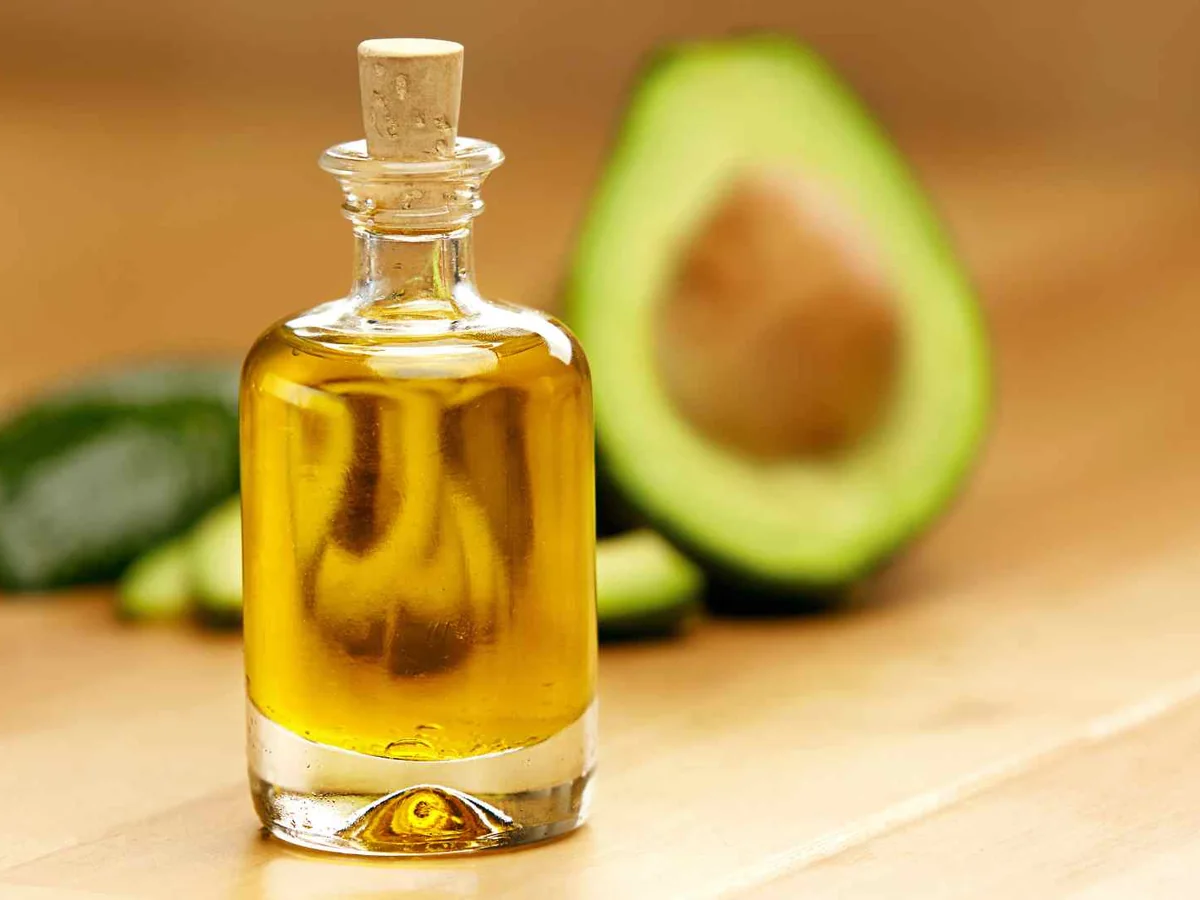 A clear bottle of golden oil beside a halved avocado