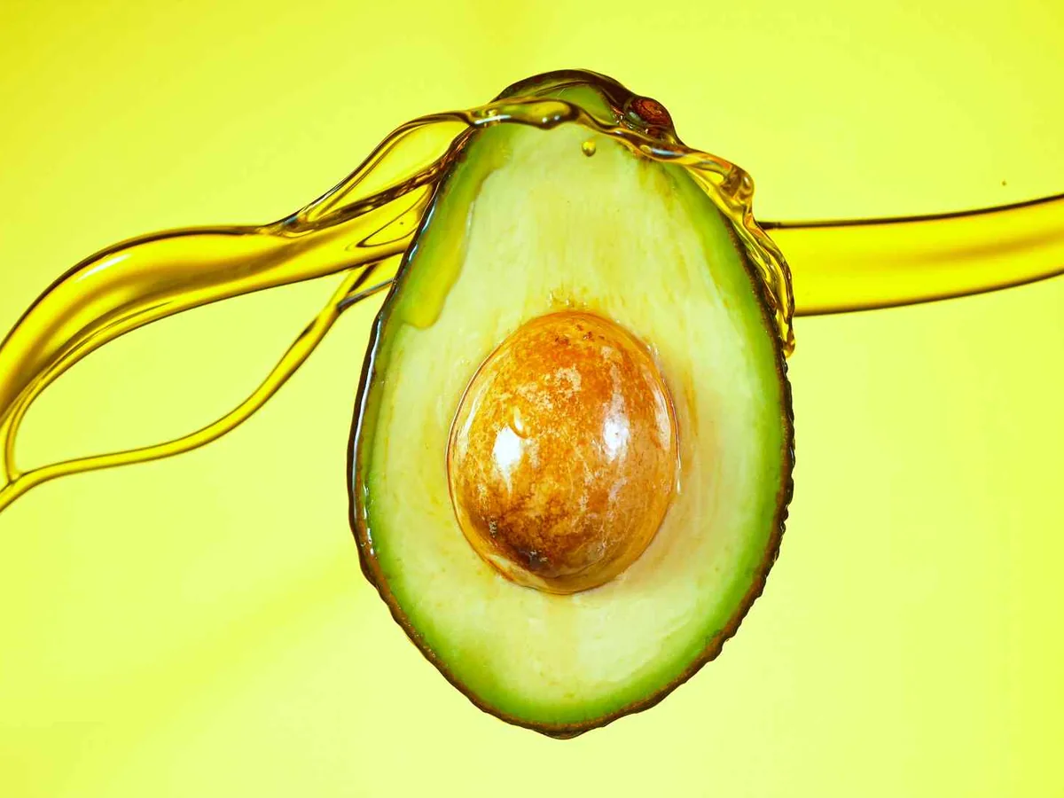 A halved avocado surrounded by a splash of golden oil