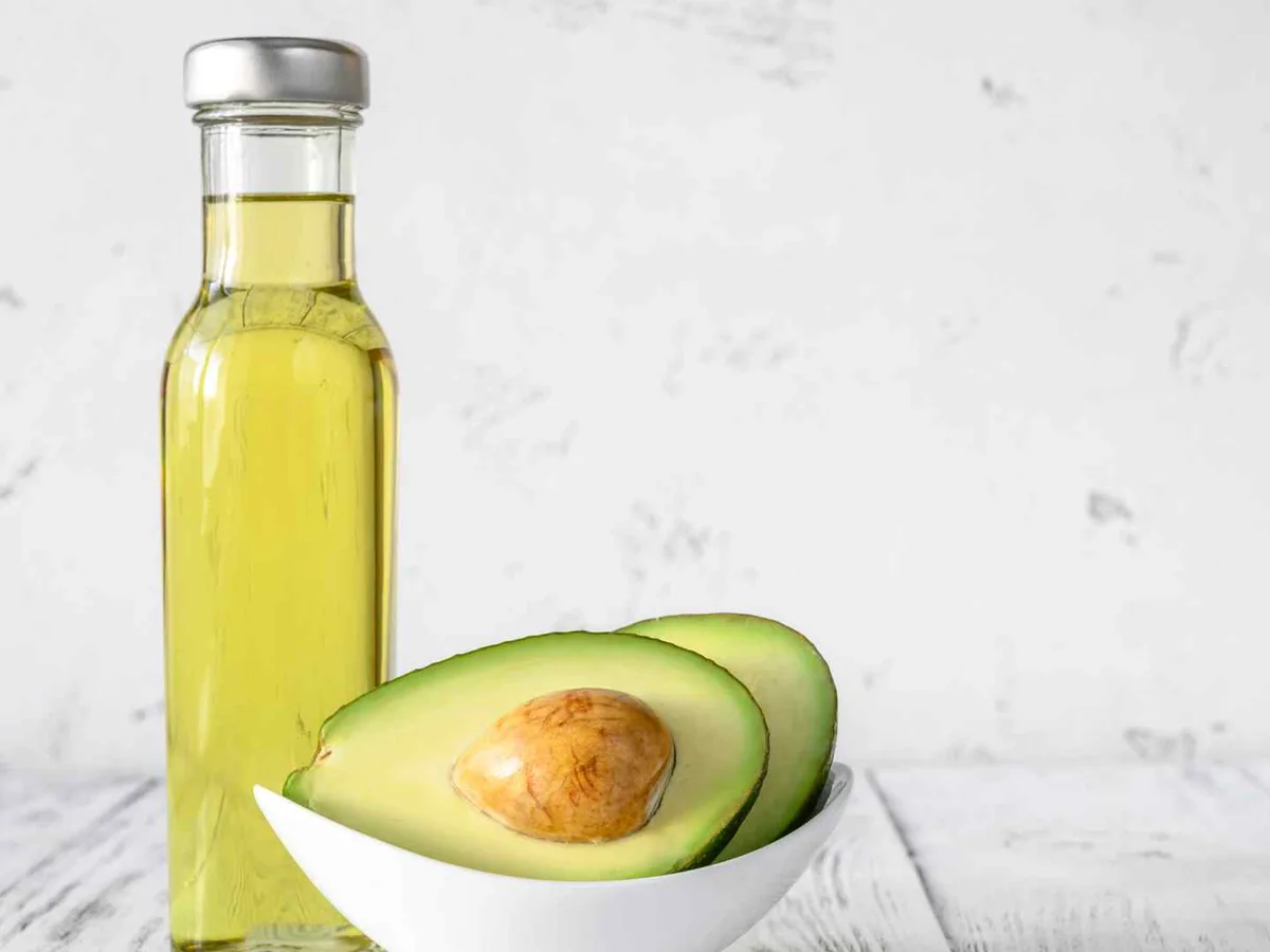 A small bottle of pale oil beside a halved avocado