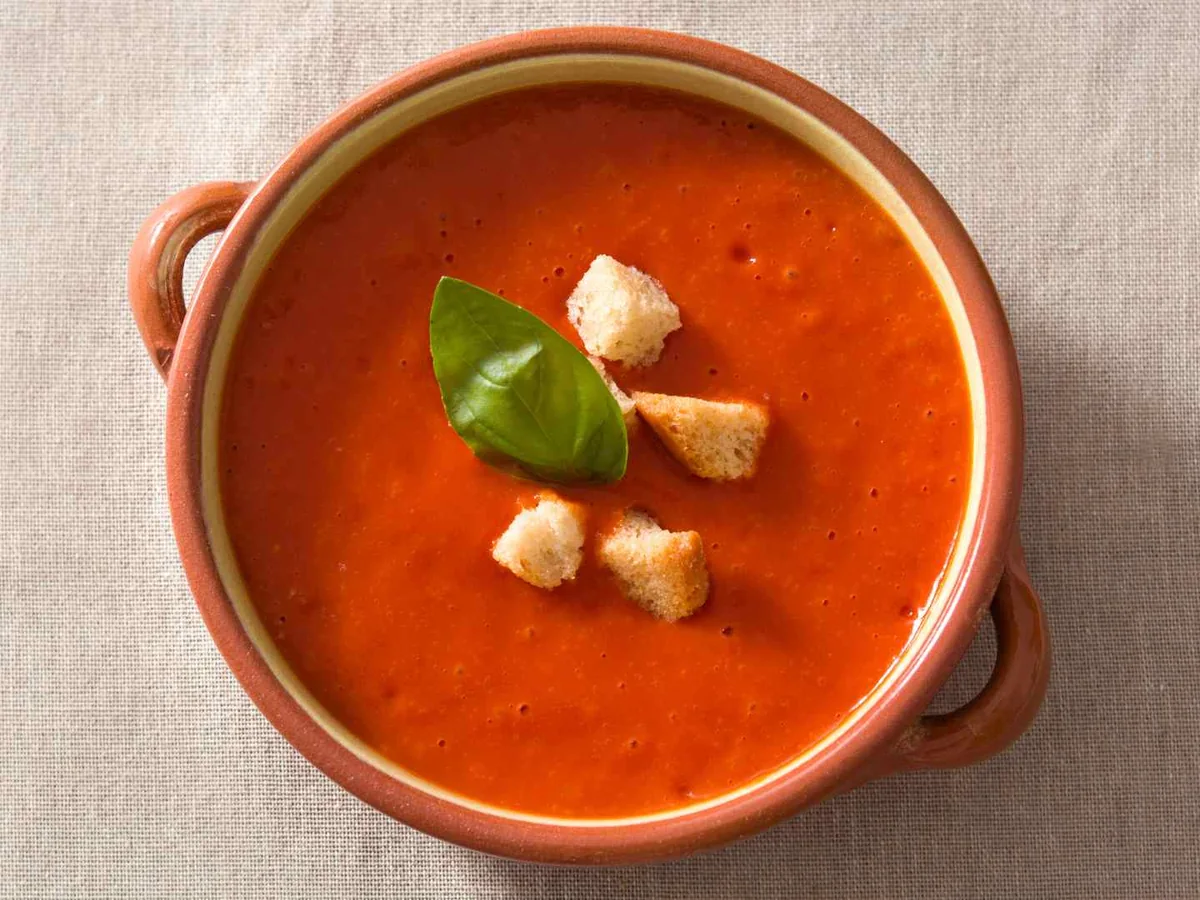 A bowl of tomato soup topped with basil and croutons