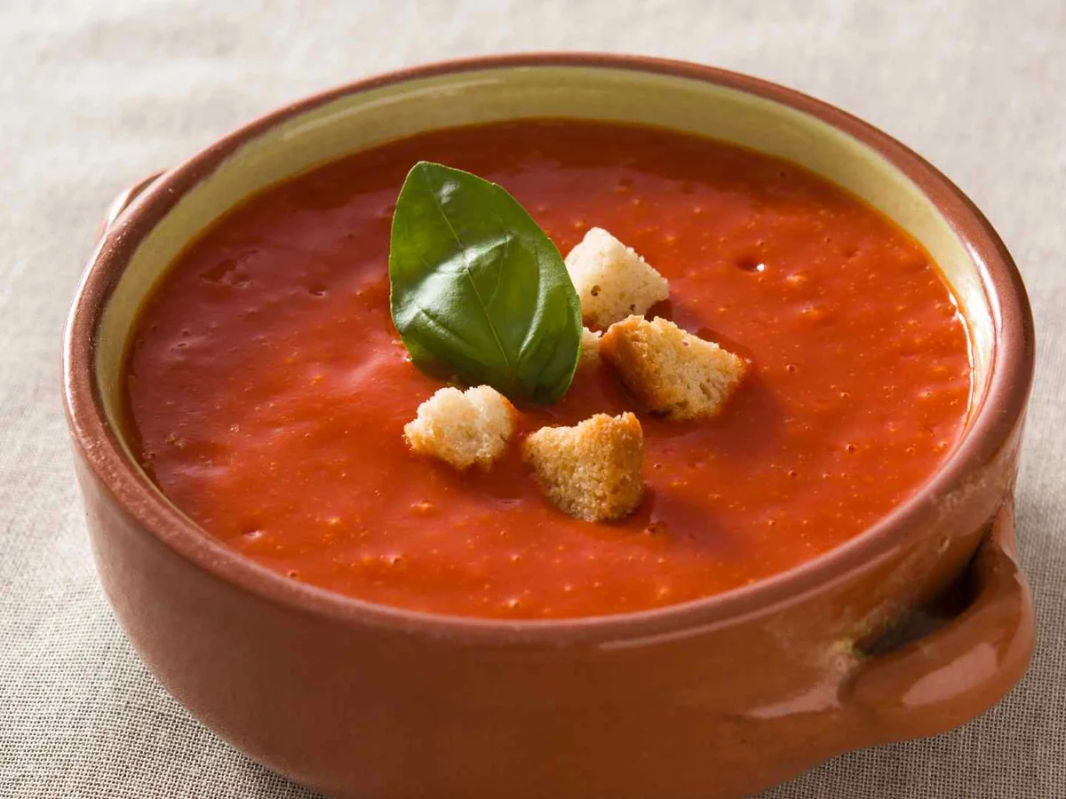 Tomato soup in a brown crock topped with basil and croutons