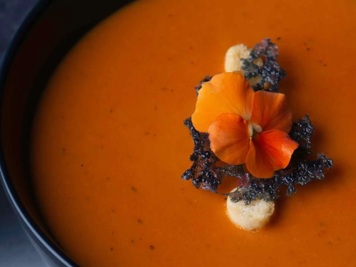 An orange-red soup topped with an edible flower