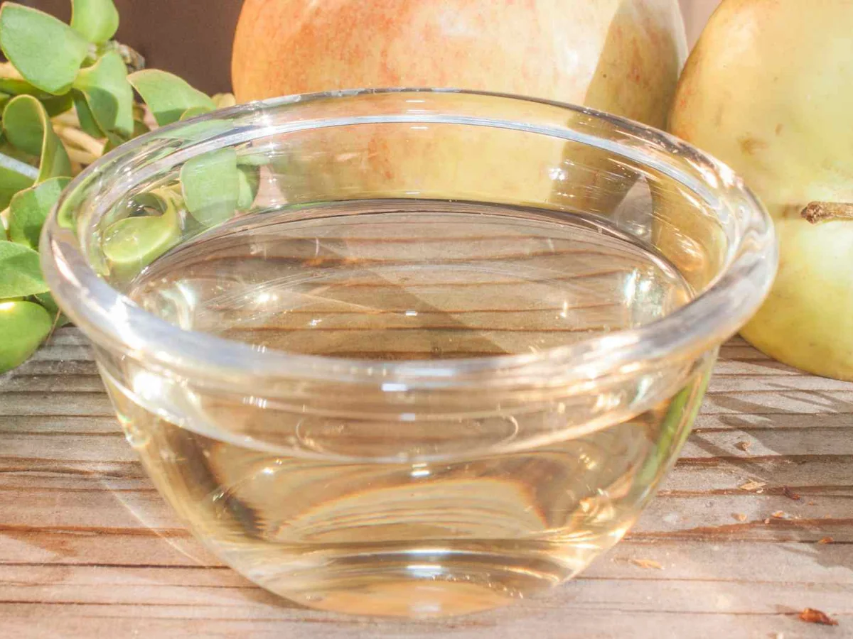Clear vinegar in a glass bowl beside onions and herbs