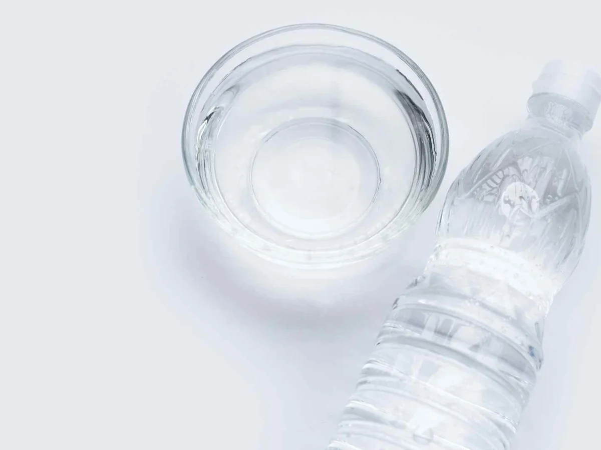 A clear bottle and bowl of colorless vinegar on white