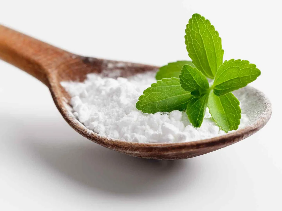 White stevia powder on a wooden spoon with green leaves