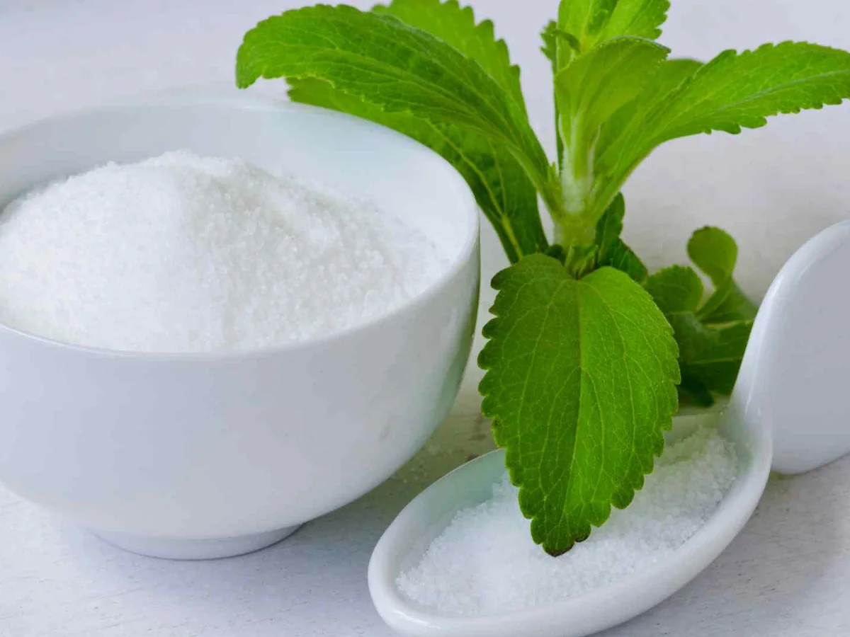White stevia powder in a bowl beside green stevia leaves