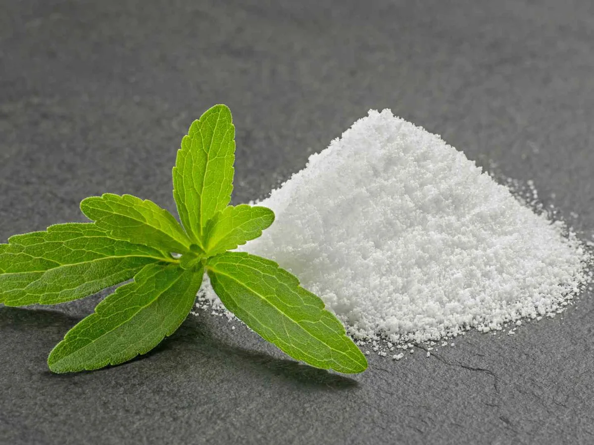 A mound of white stevia powder beside green leaves