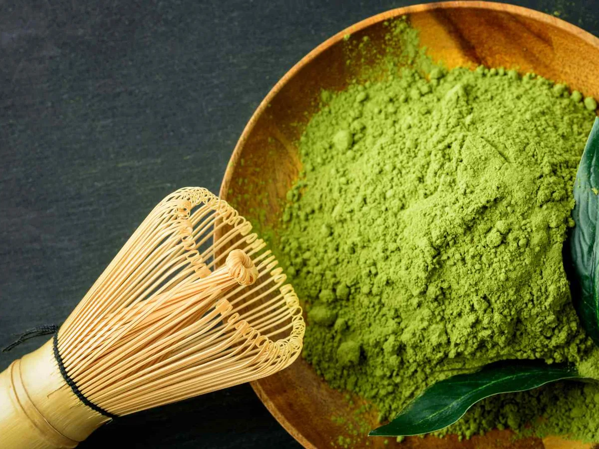 Green matcha powder in a wooden bowl with a bamboo whisk