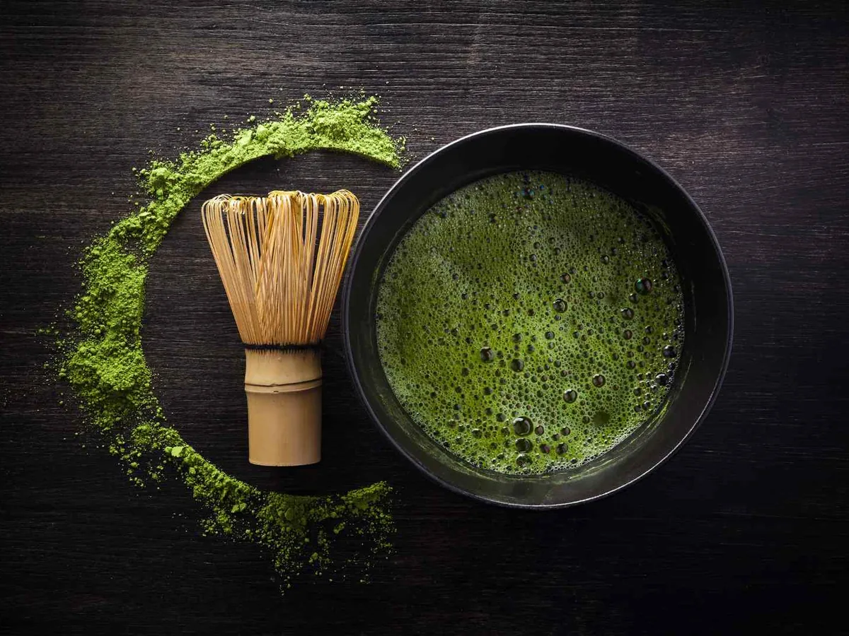 A dark bowl of prepared matcha beside a bamboo whisk